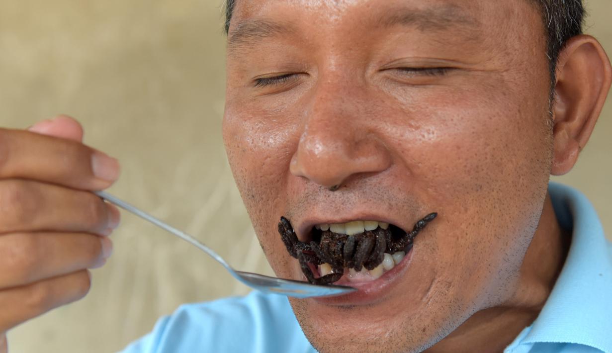 Warga lokal memperlihatkan cara menikmati tarantula goreng di wilayah Skun, Provinsi Kampong Cham, Kamboja, 14 Maret 2018.  Aping, camilan tradisional dari tarantula ini, kian langka sehingga harganya bertambah mahal. (TANG CHHIN Sothy / AFP)
