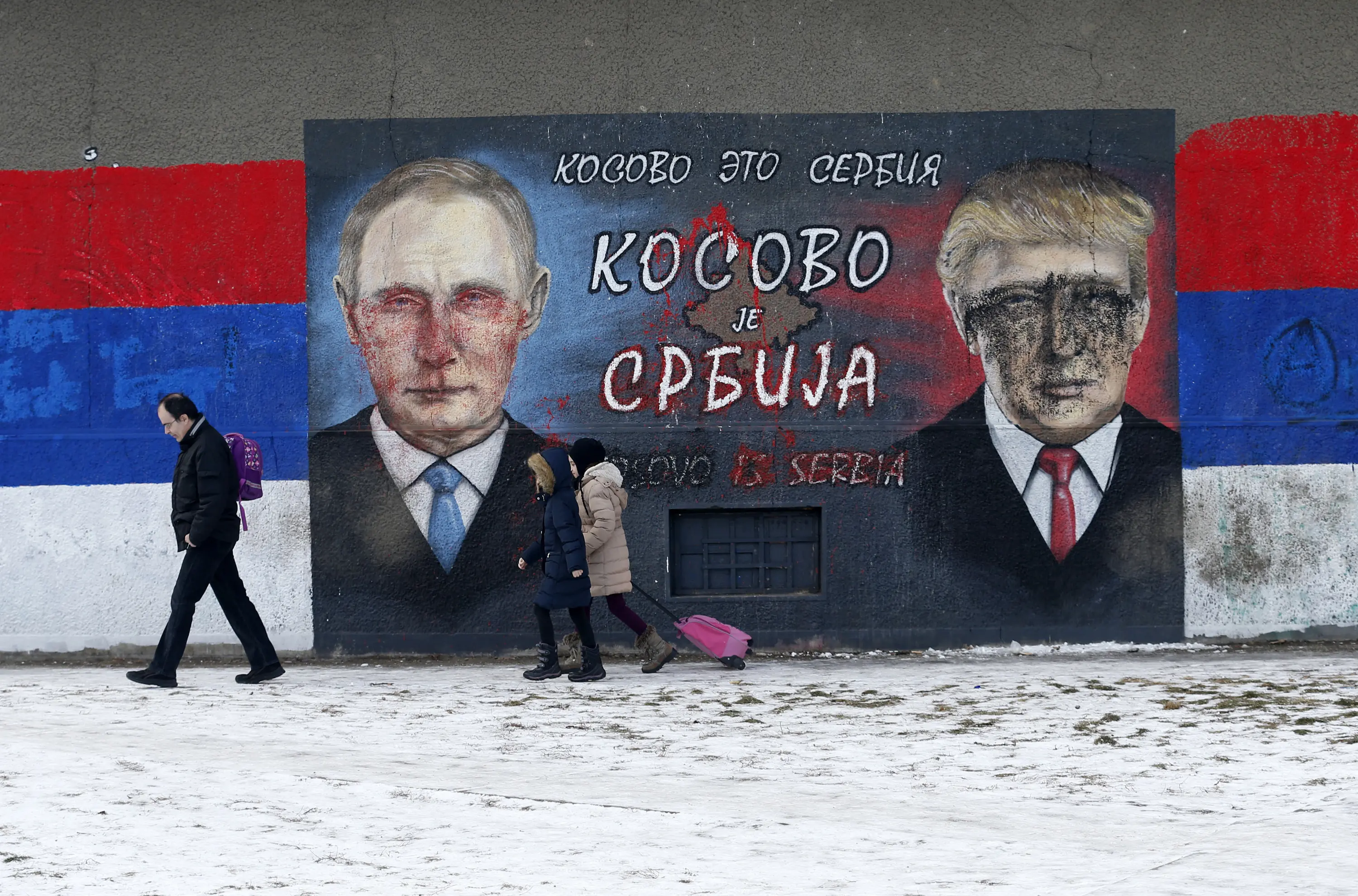 Sejumlah orang melintas di depan grafiti bergambar Donald Trump dan Vladimir Putin yang dirusak dengan cat di Belgrade, Serbia, Jumat (20/1). Diduga pelaku pengrusakan adalah mereka yang tak suka Trump menjadi Presiden AS. (AP Photo / Darko Vojinovic) 