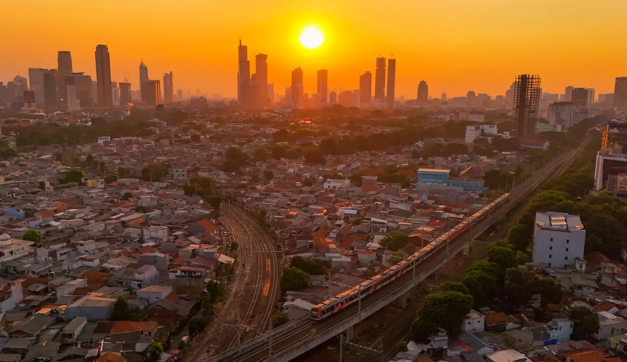Rangkaian kereta melewati kawasan padat penduduk dengan latar belakang gedung bertingkat saat matahari terbenam di kawasan Manggarai, Jakarta, Kamis, 16/07/ 2026. (KLY/ Arie Basuki)
