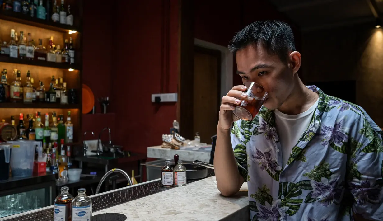 Seorang karyawan berpose sambil menikmati segelas minuman Pfizermeister, minuman yang terinspirasi oleh vaksin virus corona Covid-19, di sebuah bar koktail di George Town di pulau Penang, Malaysia (8/9/2021). (AFP/Mohd Rasfan)