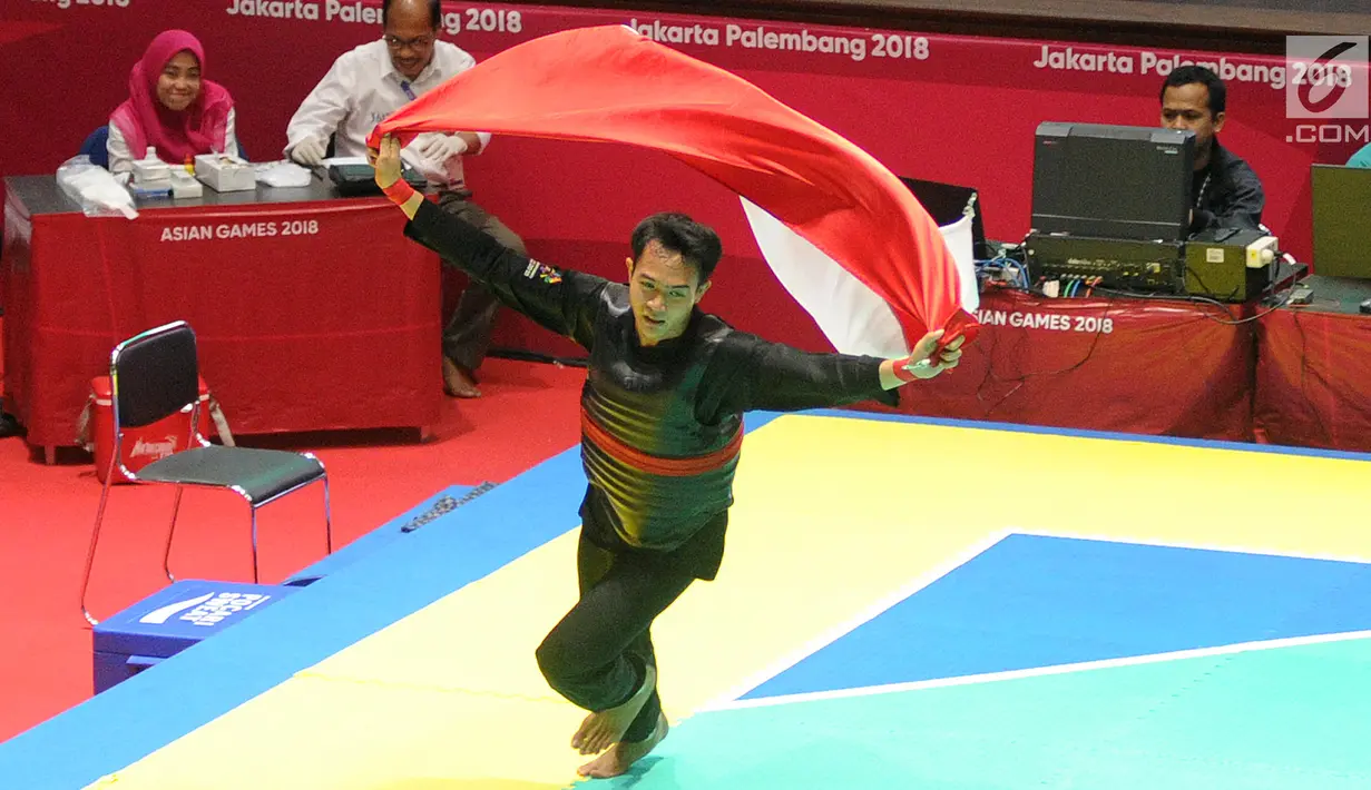 Pesilat Indonesia, Komang Harik Adi Putra mengibarkan bendera Merah Putih usai mengalahkan pesilat Malaysia Mohd Al Jufferi Jamari dalam babak final Kelas E Putra Asian Games 2018 di TMII, Jakarta, Senin (27/8). (Merdeka.com/Arie Basuki)