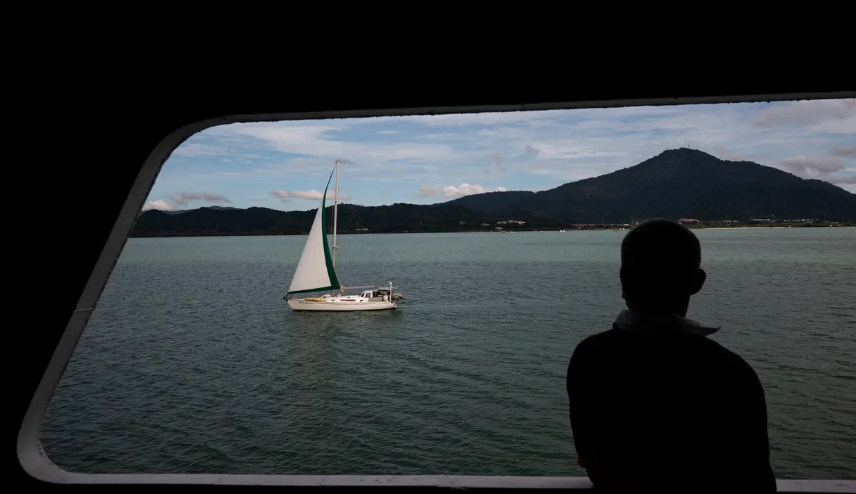 Penumpang feri melihat kapal layar di dekat pulau liburan Langkawi, yang ditutup untuk sebagian besar pengunjung luar karena penguncian sebagian yang ditetapkan  pihak berwenang untuk mengekang penyebaran Covid-19, di negara bagian Kedah, Malaysia utara (18/11/2020). (AFP/Mohd Rasfan)
