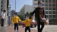Seorang wanita dan anak-anak yang mengenakan masker dan pelindung wajah berjalan di jalan di Hong Kong, Jumat (4/3/2022). Pemimpin Hong Kong awal pekan ini mengatakan mobilitas orang mungkin dibatasi selama tes covid-19 massal wajib ketika kasus harian mencapai rekor. (AP Photo/Kin Cheung)