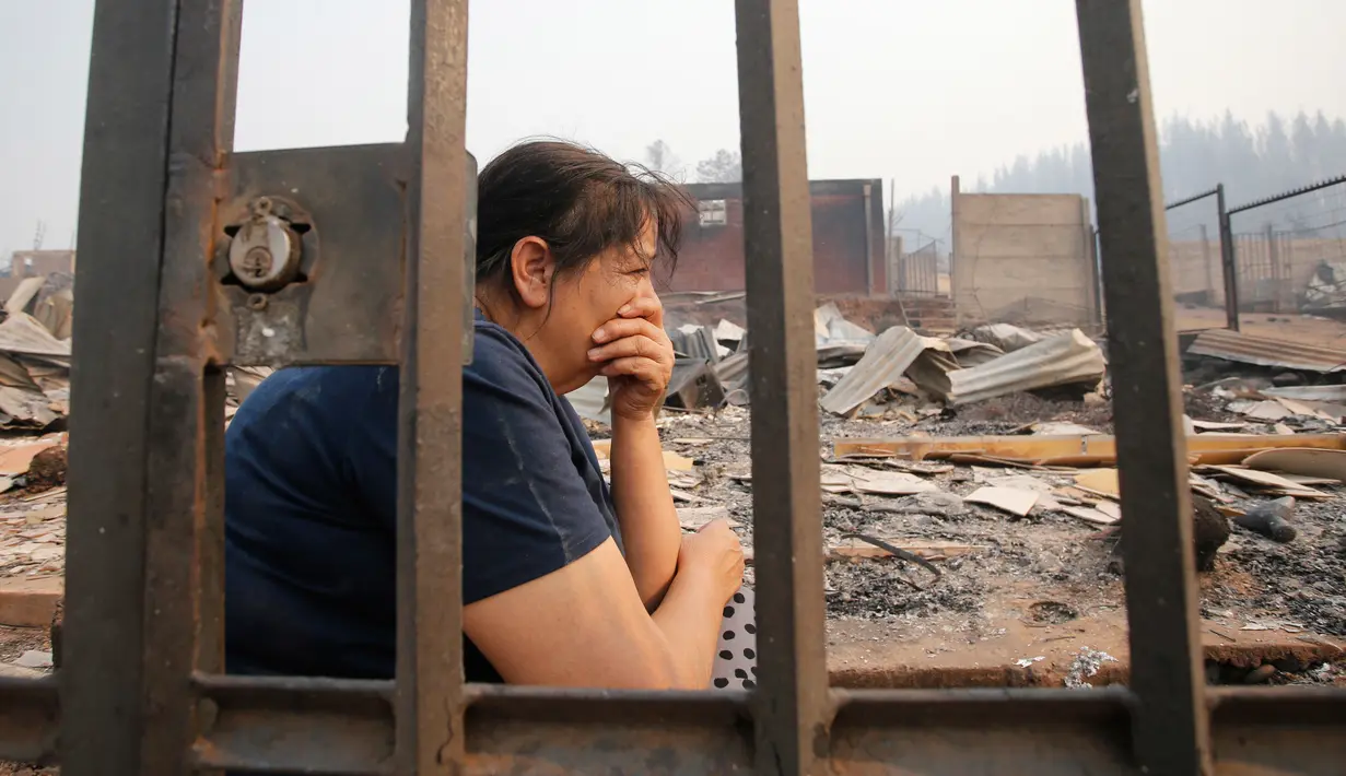 Warga duduk di sekitar puing-puing rumahnya yang terbakar di Santa Olga, Chile, (26/1). Kebakaran hutan yang terjadi dalam sepekan terakhir telah menghanguskan lahan seluas 155 kilometer persegi. (Javier Torres/Aton via AP)