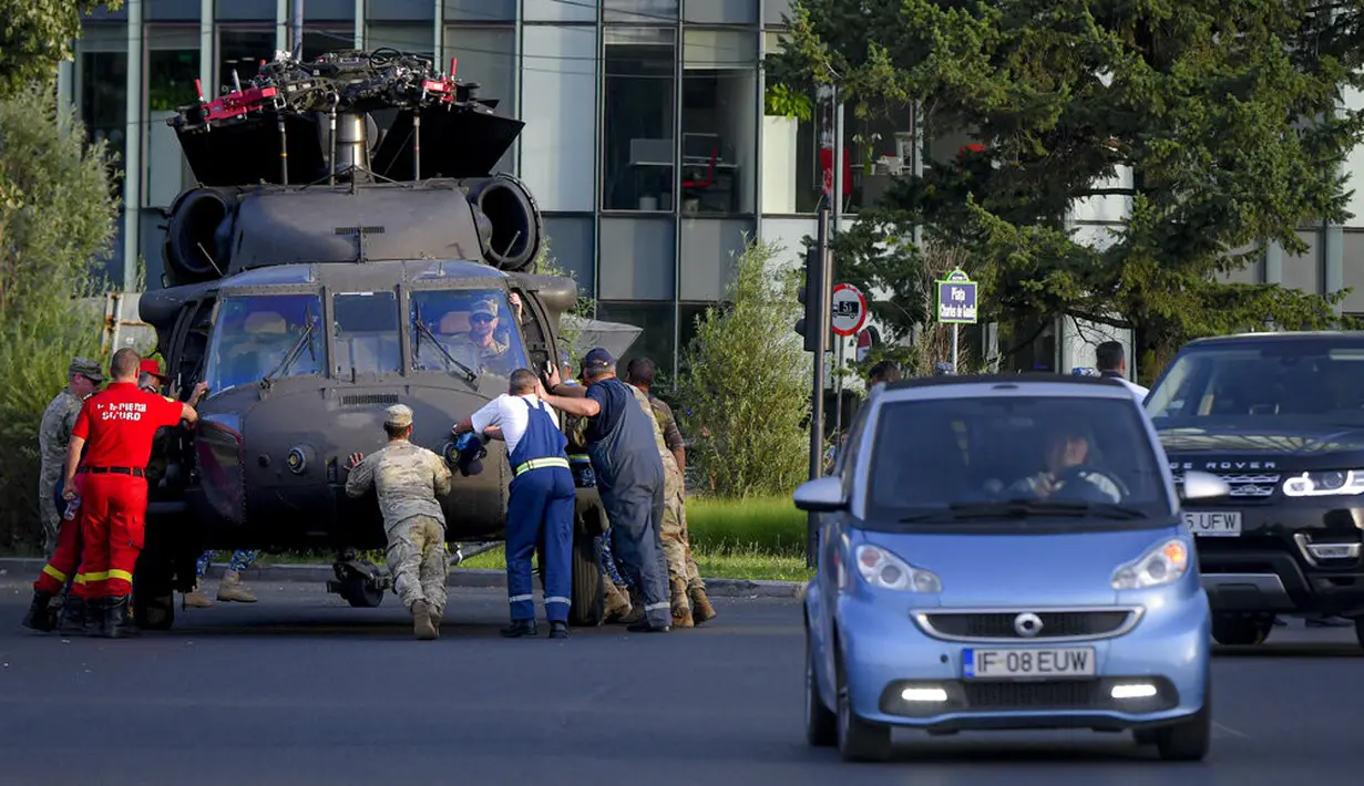Petugas servis bersiap memindahkan helikopter Black Hawk militer AS yang mendarat darurat di boulevard yang sibuk, di Bucharest, Kamis (15/7/2201). Helikopter yang ambil bagian dalam persiapan hari Penerbangan Rumania itu mendarat darurat karena masalah teknis. (AP Photo/Andreea Alexandru)