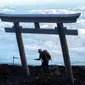 Seorang pria mencapai puncak Gunung Fuji, barat Tokyo pada 18 Juli 2021. Mendaki Gunung Fuji bukanlah hal yang mudah, tetapi pemandangan matahari terbit di atas lautan awan adalah hadiah terindah bagi yang mencapai puncak tertinggi di Jepang. (Charly TRIBALLEAU/AFP)