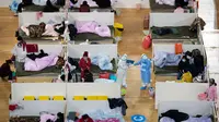 Petugas medis berjalan di antara pasien dengan gejala ringan virus corona COVID-19 yang beristirahat pada malam hari di stadion olahraga yang diubah menjadi rumah sakit darurat di Wuhan, 18 Februari 2020. Jumlah korban virus corona hingga Kamis (20/2) kembali meningkat menjadi 2.120 orang. (STR/AFP)