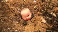 Sebuah kepala bayi terlihat berada di atas permukaan tanah dengan menunjukkan senyum menakutkan di wajahnya.