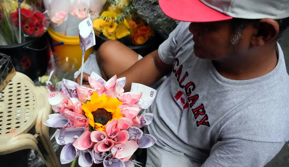 Seorang pekerja membuat karangan bunga yang terbuat dari mata uang kertas di pasar bunga di Manila, Filipina, Senin (13/2/2023). Buket tersebut merupakan bagian dari gimmick Hari Kasih Sayang oleh seorang pemilik toko bunga. (AP Photo/Aaron Favila)