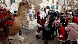Anak-anak melihat unta yang dikendarai seorang pria mengenakan busana seperti Santa Claus di sepanjang tembok Ottoman Kota Tua Yerusalem (21/12). (AFP Photo/Gali Tibbon)