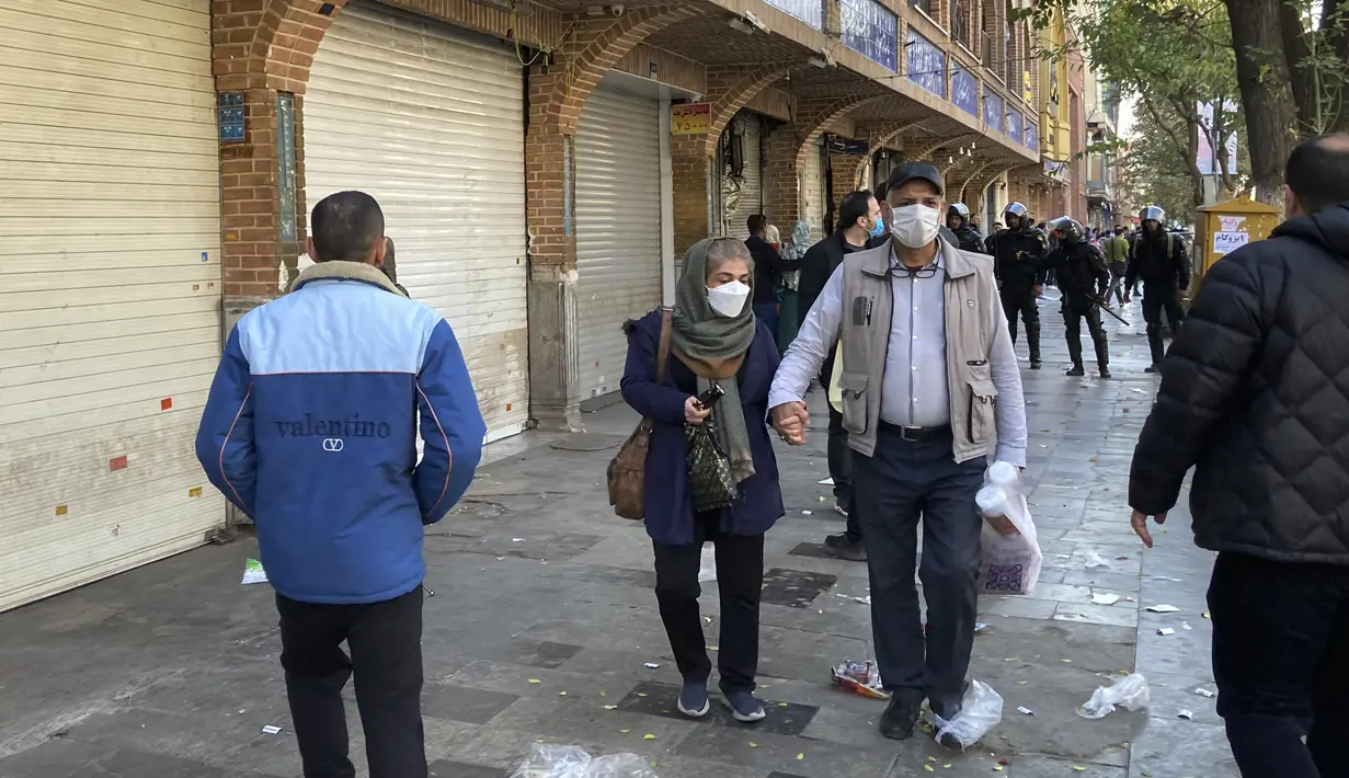 Orang-orang berjalan di depan toko-toko yang tutup di Grand Bazaar Teheran saat polisi anti huru-hara mengontrol lokasi protes, Iran, Selasa (15/11/2022). Etalase toko yang tertutup dapat dilihat di seluruh Teheran, pada hari Selasa. (AP Photo/Vahid Salemi)