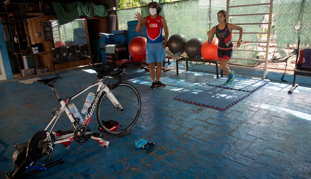 Atlet triathlon Kuba, Leslie Amat berlari dengan tali di pinggangnya di bawah pengawasan sang pelatih, Dioseles Fernandez di teras rumahnya di Havana, Senin (20/4/2020). Atlet Kuba tak bisa berlatih di fasilitas olahraga seperti biasanya selama pademi corona. (AP /Ismael Francisco)