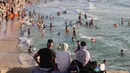 Warga Palestina mengamati pengnjung yang bermain air di pantai Beit Lahia di Jalur Gaza utara saat para siswa memulai liburan musim panas mereka pada 3 Juni 2022. Sejumlah warga menikmati musim panas dengan berenang dan bermain air di pantai. (MOHAMMED ABED / AFP)