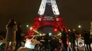 Wisatawan mengambil gambar Menara Eiffel pada Senin (16/11), yang dihiasi lampu berwarna bendera Prancis untuk menghormati para korban serangan teror di Paris pada 13 November 2015 lalu. (AFP PHOTO/LUDOVIC MARIN)
