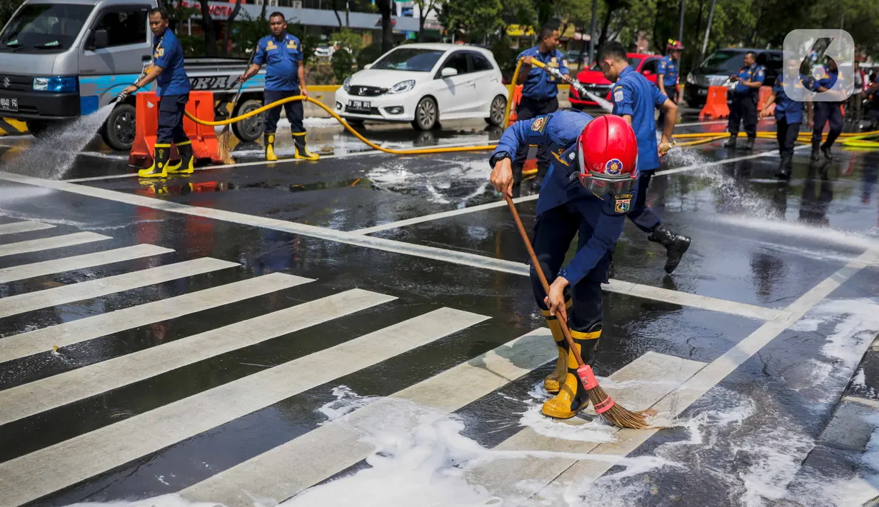 Sejumlah personil pemadam kebakaran membersihkan tumpah oli yang terjadi di Jalan Veteran depan Gedung Krida Bakti, Jakarta, Kamis (16/1/2020). Petugas damkar  melakukan pembersihan dengan cairan deterjen maupun campuran khusus agar jalan tersebut tidak lagi licin. (Liputan6.com/Faizal Fanani)