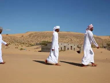 Mantan penduduk Wadi al-Murr berjalan dekat rumah-rumah terlantar di Desa Omani, Wadi al-Murr, Oman, 31 Desember 2020. Pasir yang menggunung hanya menyisakan sedikit bukti bahwa Desa Omani pernah ada di Wadi al-Murr, Oman. (MOHAMMED MAHJOUB/AFP)