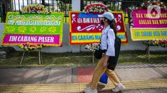 Seorang wanita melintas di depan karangan bunga yang memenuhi luar gedung DPR MPR RI, Jalan Gatot Subroto, Jakarta Pusat, Rabu(12/4/2023). (Liputan6.com/Faizal Fanani)