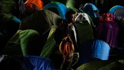 Seorang pria berjalan di sekitar tenda sementara di samping kanal di Paris, Prancis (30/5). Mereka yang menggelar tenda dibawan jembatan ini melebar hingga ke area pejalan kaki dan pengendara sepeda. (AP/Thibault Camus)