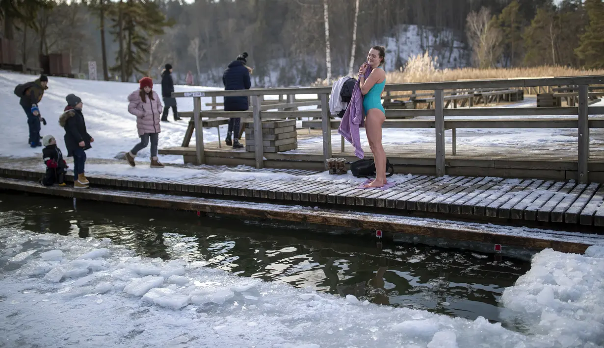 Seorang wanita mengeringkan dengan handuk setelah mandi di air es danau dekat Vilnius, Lithuania, Minggu (13/2/2022). Suhu udara 0 derajat Celcius (32 derajat Fahrenheit). (AP Photo/Mindaugas Kulbis)