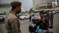 Petugas Satpol PP mengimbau pengguna kendaraan saat melakukan Pengawasan Pelaksanaan PSBB di kawasan Bundaran HI, Jakarta, Senin (13/4/2020). Petugas juga mengimbau mengatur posisi duduk dan pembatasan penumpang untuk kendaraan bermobil baik pribadi maupun angkutan umum. (Liputan6.com/Faizal Fanani)