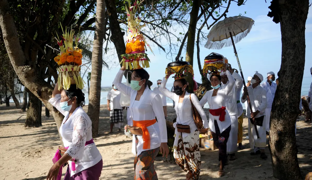 Umat Hindu membawa persembahan saat upacara Melasti menjelang Hari Raya Nyepi di Pantai Kuta, Bali (11/3/2021). Upacara Melasti dilakukan oleh perwakilan desa adat dengan jumlah terbatas serta menerapkan protokol kesehatan untuk mencegah penyebaran pandemi COVID-19. (AFP/Sonny Tumbelaka)