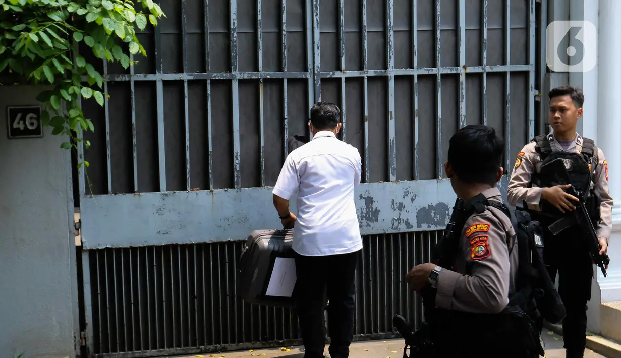 Penyidik kepolisian dengan membawa koper berwarna abu-abu gelap memasuki rumah dengan pagar dihiasi tumbuhan menjalar itu. (Liputan6.com/Herman Zakharia)