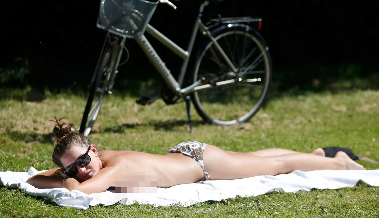 Seorang wanita berjemur di atas terik matahari di Regents Park, London, Inggris, Selasa (19/7). Inggris tengah dilanda gelombang panas dengan suhu 35 derajat celcius. (REUTERS/Neil Hall)