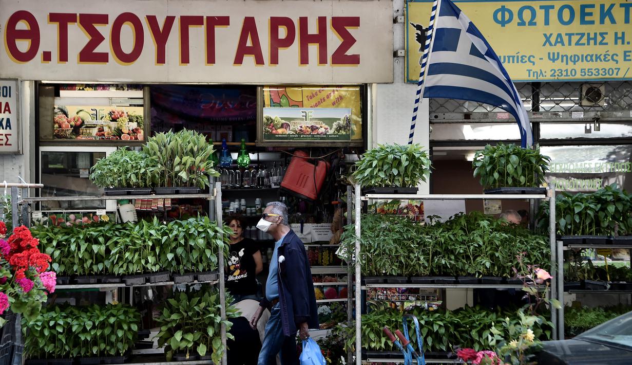 Seorang pejalan kaki berjalan di jalan mengenakan masker di pusat Thessaloniki, Yunani utara (18/5/2022). Sebuah komite ahli dari Kementerian Kesehatan sedang memeriksa kemungkinan melonggarkan mandat masker pada 1 Juni, menyusul penurunan Covid19. (AFP/Sakis Mitrolidis)