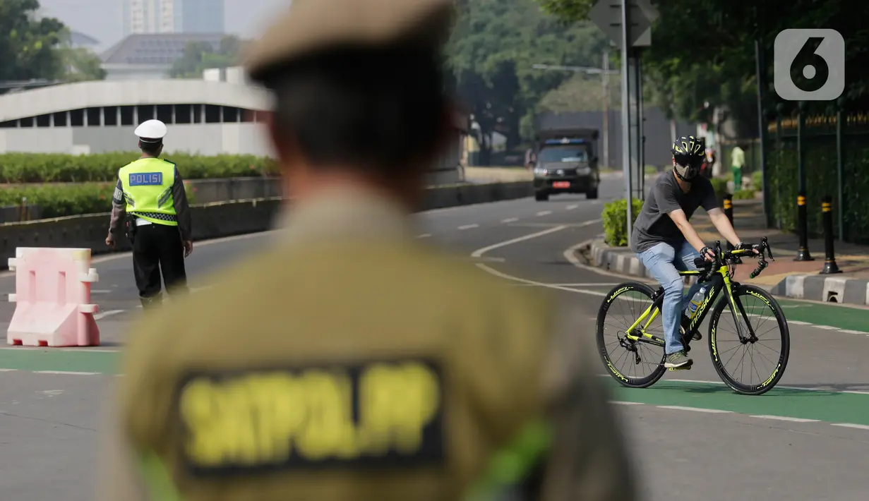 Petugas gabungan melakukan pengalihan jalur pesepeda di kawasan Sudirman-Thamrin, Jakarta, Minggu (5/9/2021). Pemberlakuan jalur ganjil genap pada masa PPKM membuat pengguna sepeda dilarang melintasi kawasan ganjil-genap pagi ini. (Liputan6.com/Angga Yuniar)