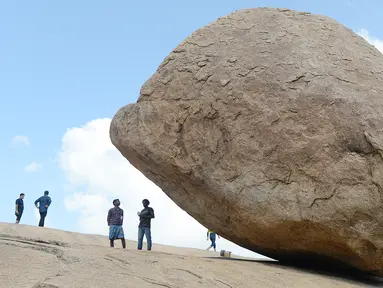 Pengunjung berdiri dekat batu 'Krishna's Butter Ball' yang terkenal di Mahabalipuram, India, Kamis (3/10/2019). Batu yang dikenal masyarakat sekitar dengan nama Vaan Irai Kal ini terletak di lereng dengan kemiringan 45 derajat. (ARUN SANKAR / AFP)