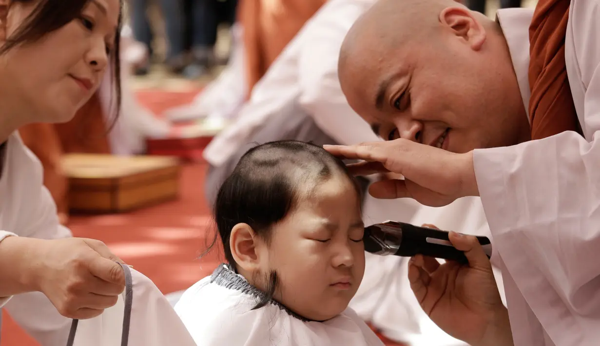 Ekspresi Seorang anak lelaki bernama Budha Myung Bub saat rambutnya dicukur oleh seorang biksu selama kebaktian merayakan ulang tahun ke-2.563 Buddha pada 12 Mei, di Kuil Jogye di Seoul, Korea Selatan, Senin (22/4). Sepuluh anak terpilih menjadi peserta peringatan ini. (AP Photo/Ahn Young-joon)