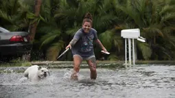 Darcelle Jacobs dan anjingnya berjalan dalam banjir di sepanjang jalan Pantai Fort Myers, Florida, Senin (31/7). Untungnya, tidak ada korban jiwa akibat badai tropis Emily. (The News-Press via AP/Andrew West)