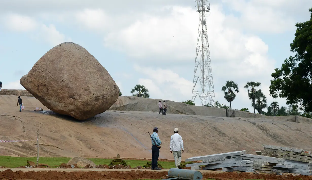 Pengunjung berdiri dekat batu 'Krishna's Butter Ball' di Mahabalipuram, India, Kamis (3/10/2019). Menurut mitos masyarakat Hindu posisi batu itu dikaitkan legenda Dewa Krishna yang berusaha mencuri mentega dari dalam toples milik ibunya. (ARUN SANKAR / AFP)