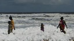 Penduduk setempat berjalan di atas limbah busa yang disebabkan polutan saat bercampur dengan ombak di pantai di Chennai (29/11/2019). Limbah busa tersebut  membuat penduduk dan pengunjung pantai merasa sakit. (AFP/Arun Sankar)
