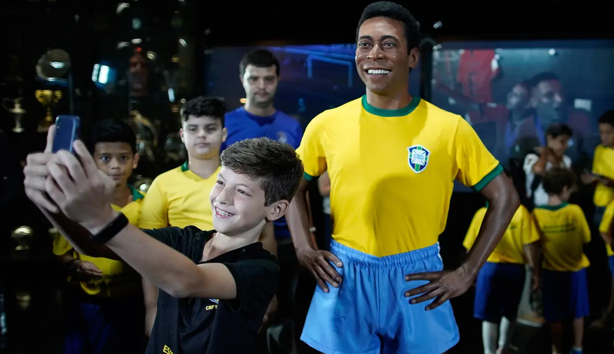 Seorang anak berswafoto dengan patung pemain sepak bola legendaris Brasil, Pele, di Museum Tim Sepak Bola Brasil di Rio de Janeiro, Kamis (20/2/2020). Konfederasi Sepak Bola Brasil meluncurkan patung Pele sebagai bagian dari peringatan 50 tahun sejak kemenangan Piala Dunia 1970. (AP/Leo Correa)