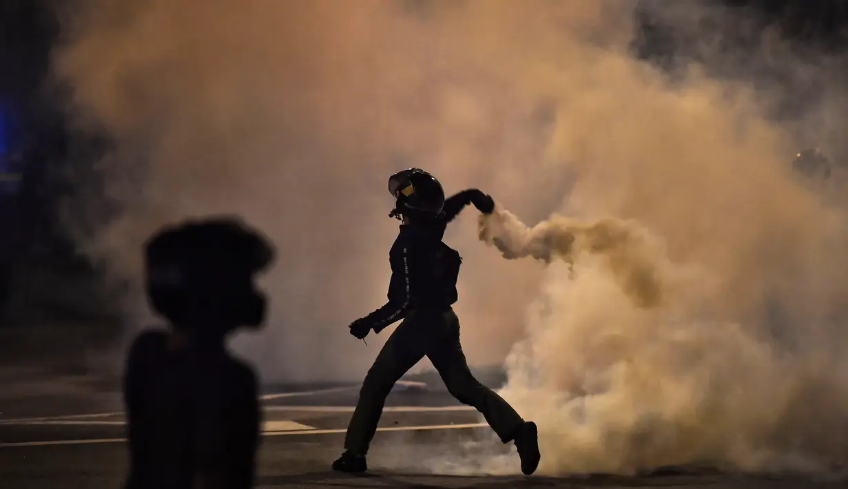 Seorang pengunjuk rasa melemparkan tabung gas air mata selama bentrokan dengan polisi di Bangkok, Thailand, Minggu (6/9/2021). Mereka memprotes ketidaksetujuan terhadap cara pemerintah Thailand menangani pandemi dan pemberian vaksin Covid-19. (AFP/Jack Taylor)