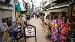 Seorang wanita mengendarai sepeda membawa anak-anaknya melihat ke arah sejumlah wanita yang mengenakan pakaian tradisional yang berbelanja di jalan Yanaka ginza di pusat Tokyo (30/9/2019). Wilayah Yanaka di ibukota Jepang dikenal sebagai salah satu yang paling kuno dan unik. (AFP Photo/Odd Andersen)