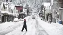 Seorang warga berjalan saat hujan salju di sepanjang Broad Street di Nevada City, California (27/12/2021). Hujan salju dingin membuat perjalanan hampir tidak mungkin dilakukan di beberapa bagian California, Nevada. (Elias Funez/The Union via AP)