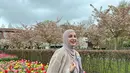 Liburan di Belanda, Shireen Sungkar tampil menawan pakai coat dan rok pleats nuansa pink sambil pose di depan bunga tulip. [Foto: IG/shireensungkar].