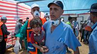 Petugas medis menggendong seorang anak Palestina yang terkena gas air mata selama protes di dekat Beit Lahiya, Jalur Gaza, Senin (14/5). Tentara Israel menembak dan membunuh puluhan warga Palestina selama protes massal di perbatasan Gaza (AP/Dusan Vranic)