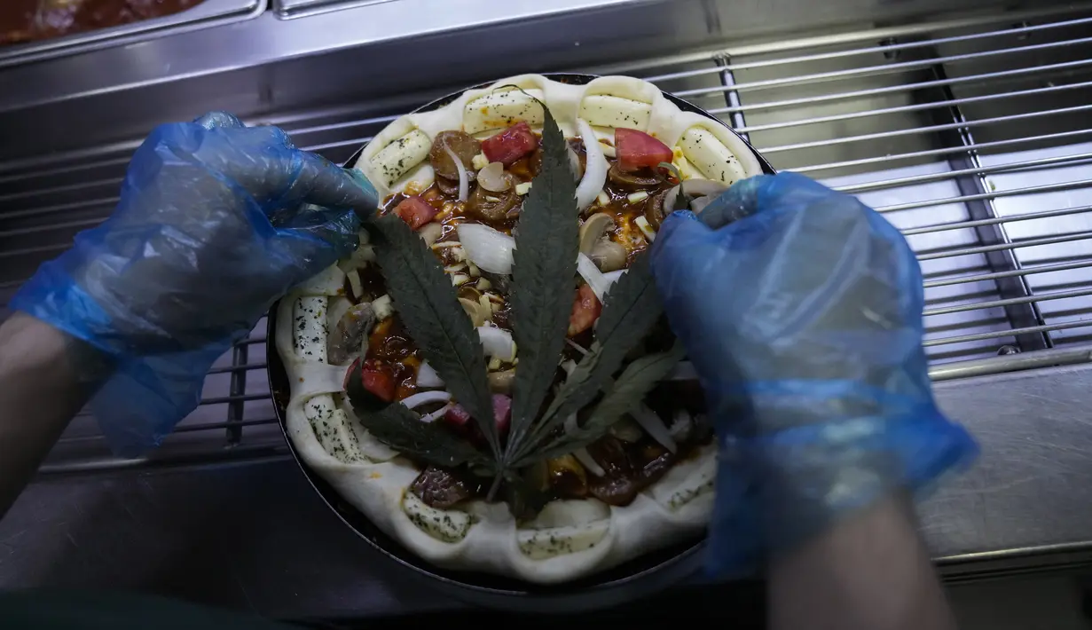 Daun ganja ditaruh di atas pizza di sebuah restoran di Bangkok, Thailand pada 24 November 2021. Produk ini menggunakan daun ganja dan legal untuk dikonsumsi, di mana seloyang pizza ganja berukuran 22 cm dihargai 499 baht atau Rp213 ribu. (AP Photo/Sakchai Lalit)