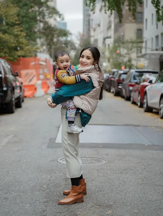 Menggendong Rayyanza, Nagita Slavina tampil chic mengenakan jaket parasut berwarna hijau yang ditumpuknya dengan puffer vest cokelat yang serasi dengan celananya. [Foto: Instagram/raffinagita1717]