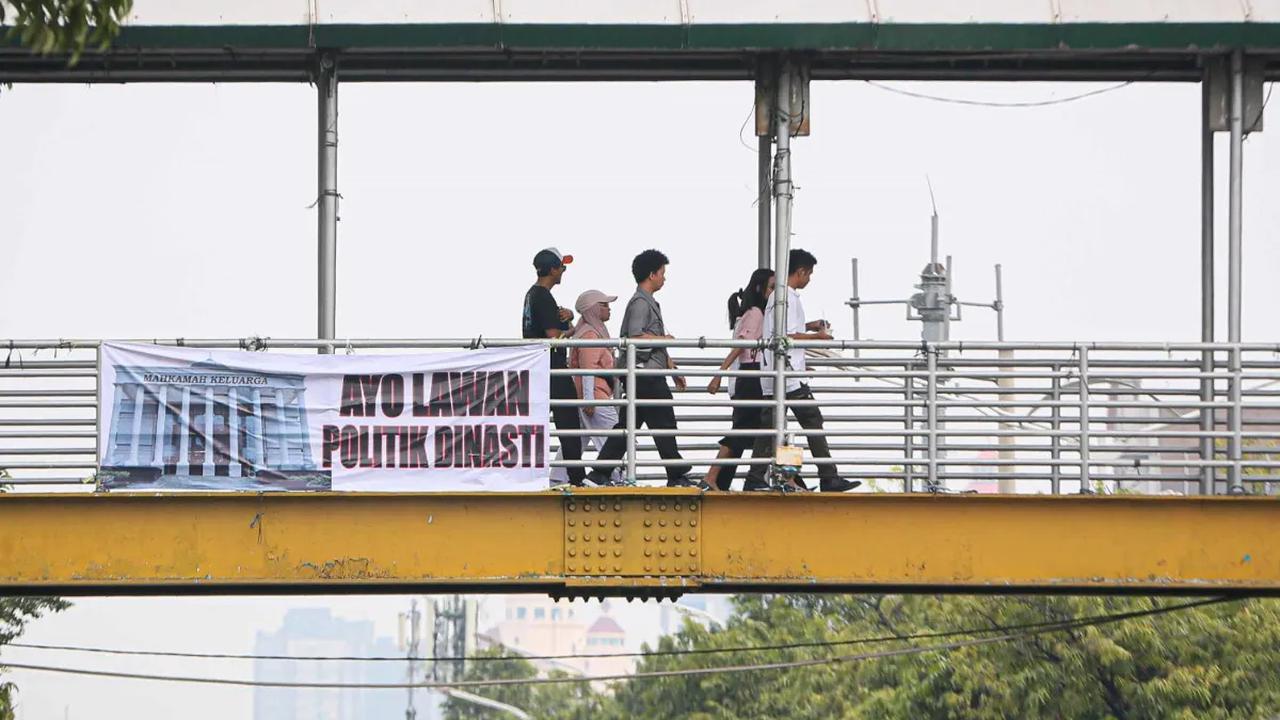 Sejumlah warga berjalan pada jempatan penyeberangan orang yang terdapat sebuah spanduk bertuliskan "Ayo Lawan Politik Dinasti" di Jakarta, Minggu (15/10/2023).