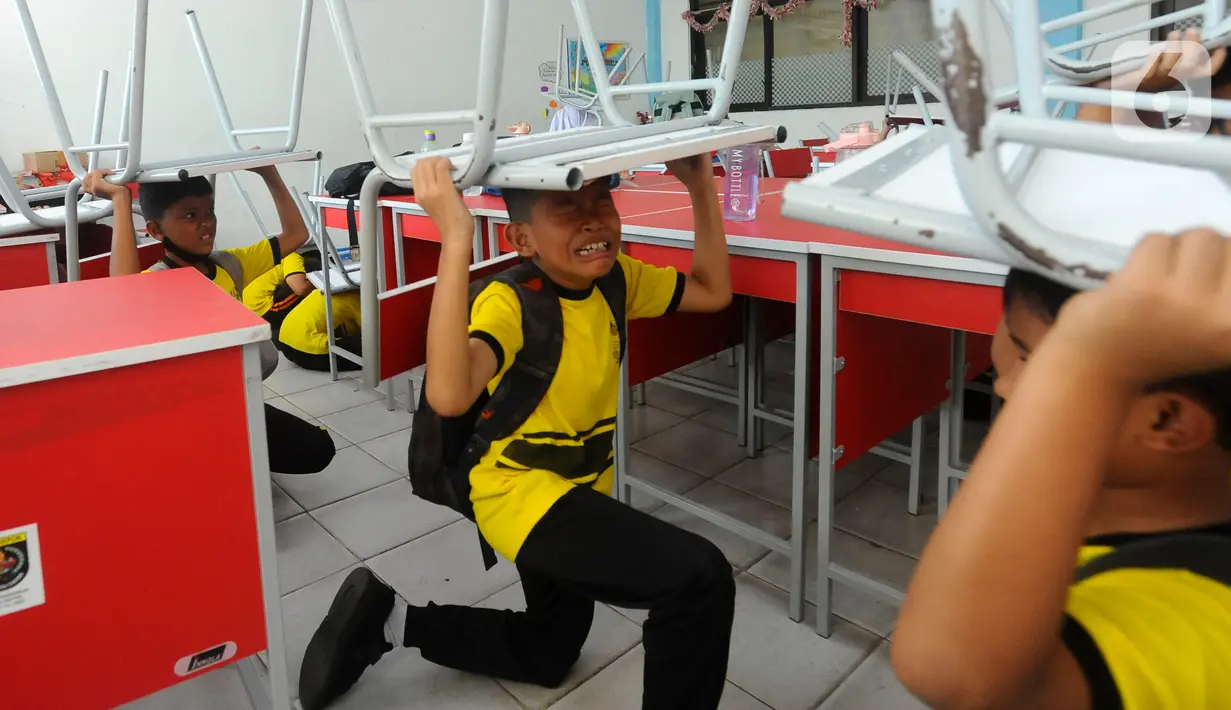 Pelajar SD Negeri Anyelir 1 berlindung di bawah meja saat mengikuti simulasi penanganan bencana alam gempa bumi di depok, jawa Barat, Kamis (20/07/2023). (merdeka.com/Arie Basuki)