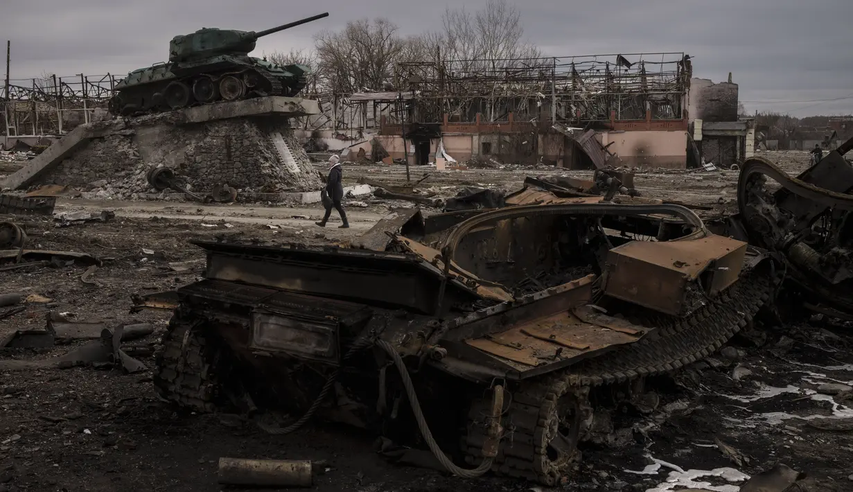Seorang perempuan berjalan melewati tank yang hancur di kota Trostyanets, Ukraina, Senin, 28 Maret 2022. Trostsyanets baru-baru ini direbut kembali oleh pasukan Ukraina setelah dikuasai oleh Rusia sejak awal perang. (AP Photo/Felipe Dana)
