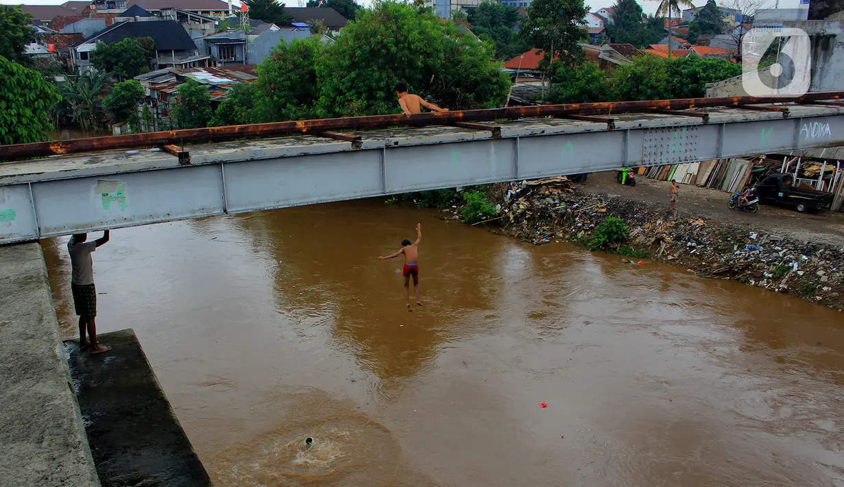 Seorang anak nekat melompat dari jembatan ke Kali Ciliwung Kalibata, Jakarta, Selasa (25/2/2020). Kali Ciliwung meluap usai hujan deras mengguyur Jakarta dan sekitarnya pada kemarin malam. (merdeka.com/magang/Muhammad Fayyadh)