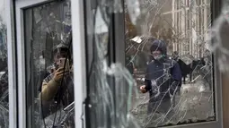 Seorang pria mengambil foto dari jendela kios polisi yang dirusak oleh demonstran selama protes di Almaty, Kazakhstan, Rabu (5/2/2022). Demonstran yang menolak kenaikan harga gas cair bentrok dengan polisi di kota terbesar Kazakhstan dan mengadakan protes di sekitar kota. (AP Photo/Vladimir Tretyako