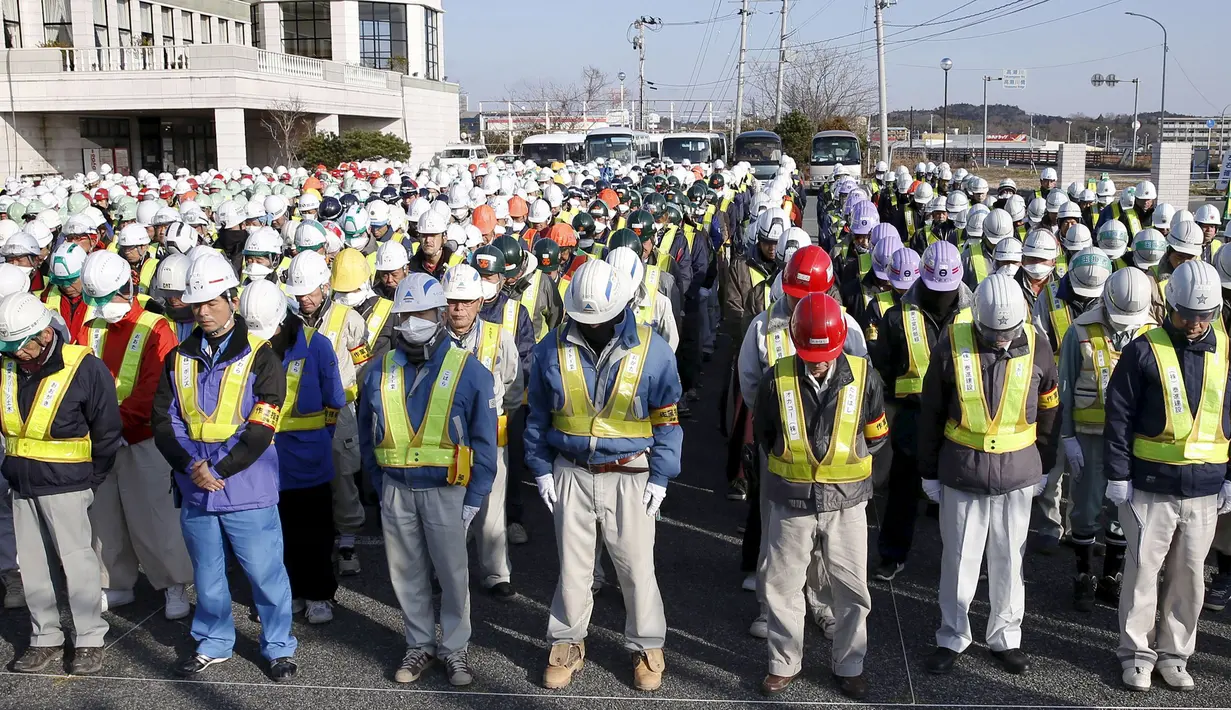 Sejumlah pekerja mengheningkan cipta untuk mengenang para korban bencana gempa dahsyat dan tsunami besar di Jepang pada 11 Maret 2011 silam, sebelum memulai pekerjaan mereka di Namie, Prefektur Fukushima, Jumat (11/3/2016). (REUTERS / Kyodo)