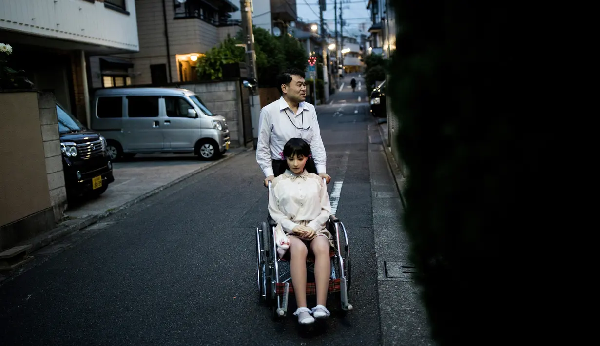 Masayuki Ozaki berjalan bersama boneka seksnya yang berada di kursi roda di Tokyo, Jepang (9/6). Ozaki mengaku, ia merasa jatuh cinta pada pandangan pertama saat melihat Mayu di ruang pameran. (AFP photo/Benrouz Mehri)