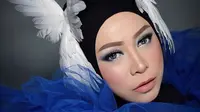 Wanita berusia 45 tahun ini tampil menggunakan headpiece berbentuk burung cendrawasih berwarna putih dipadukan dengan hijab berwarna hitam dan baju warna biru yang mengembang. (Liputan6.com/IG/@melly_goeslaw)